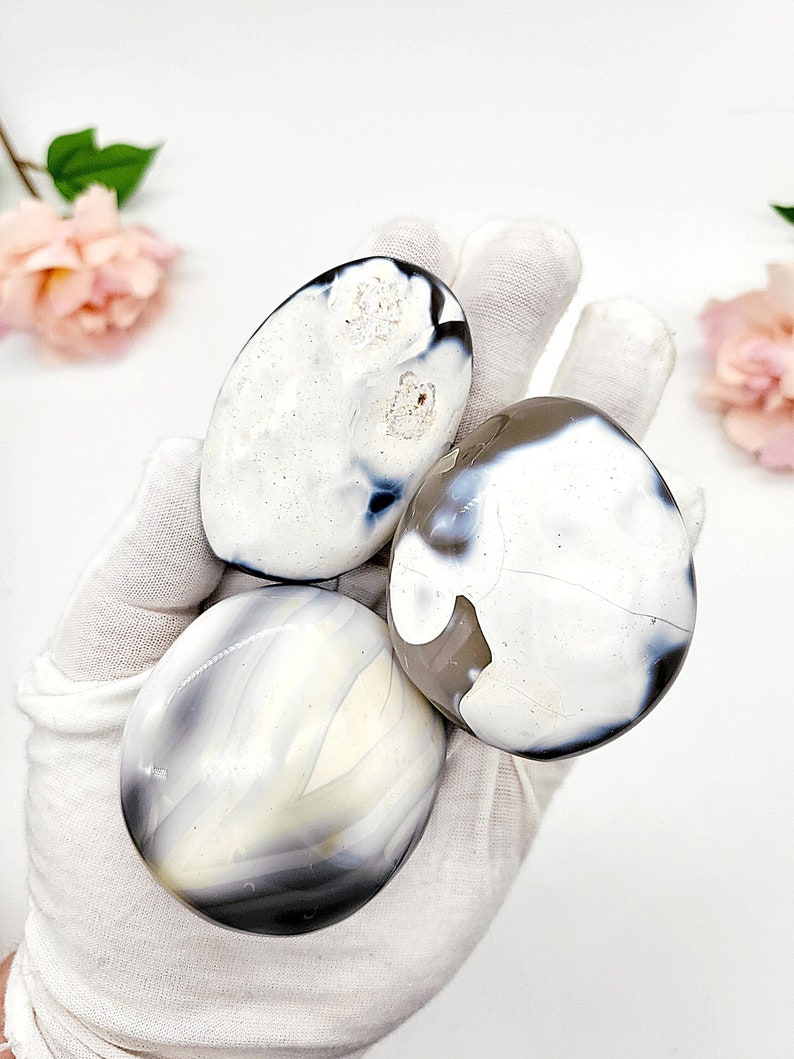 May include: Three white agate stones with gray and blue banding. The stones are smooth and polished, and they are arranged in a pile.