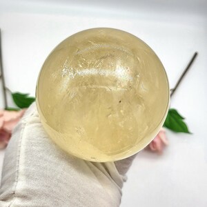 May include: A large, smooth, yellow citrine sphere. The sphere is polished and has a translucent appearance.