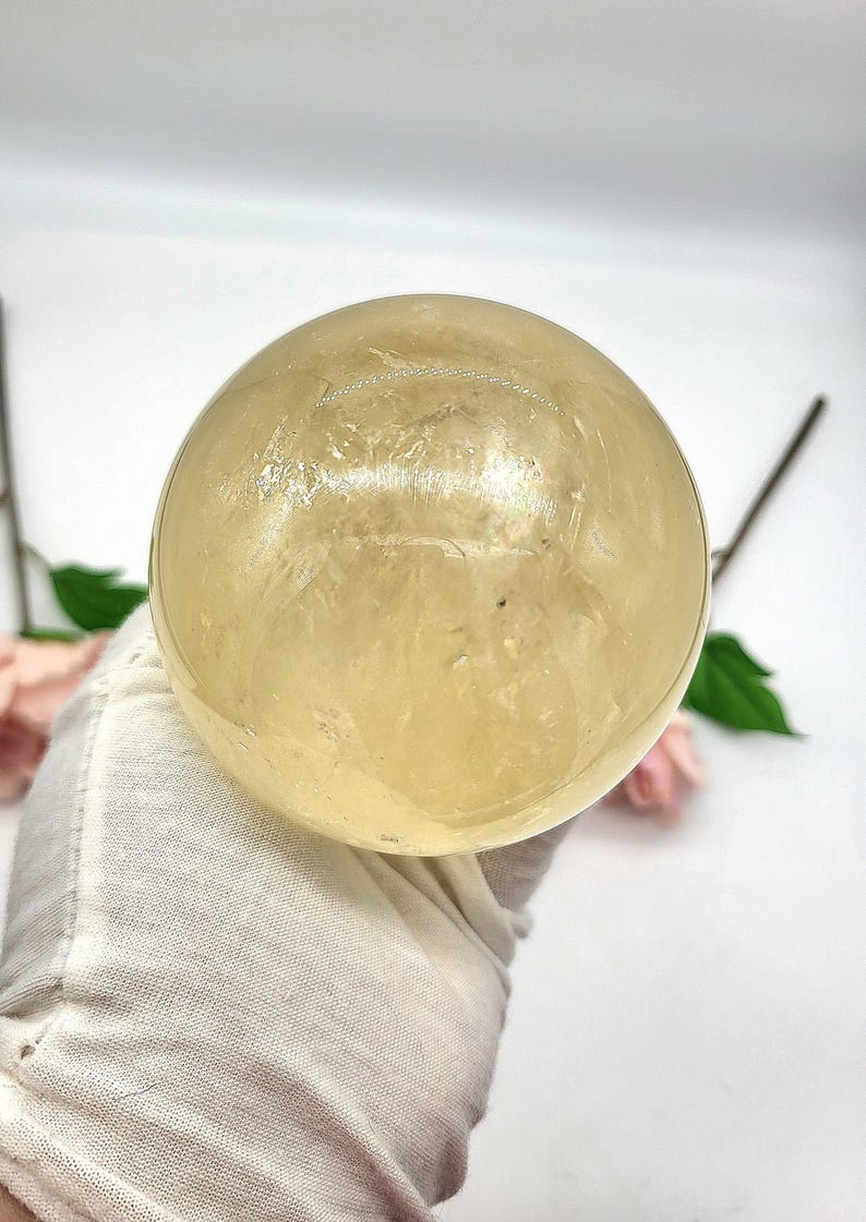 May include: A large, smooth, yellow citrine sphere. The sphere is polished and has a translucent appearance.