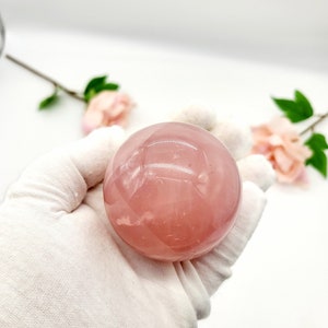 May include: A smooth, pink rose quartz sphere. The sphere is polished and has a translucent appearance.