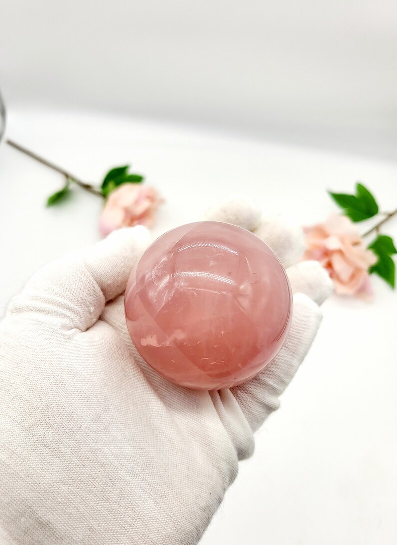 May include: A smooth, pink rose quartz sphere. The sphere is polished and has a translucent appearance.