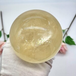 May include: A large, clear, yellow citrine crystal sphere. The sphere is smooth and polished, with a slight iridescent sheen.