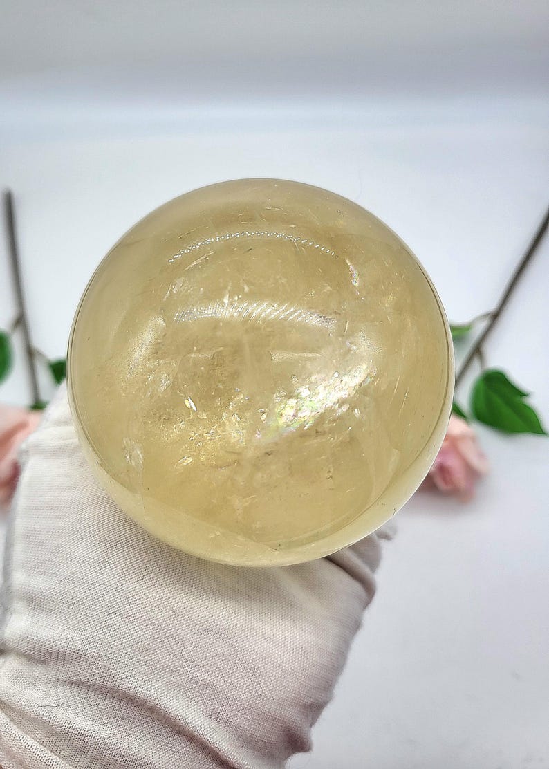May include: A large, clear, yellow citrine crystal sphere. The sphere is smooth and polished, with a slight iridescent sheen.