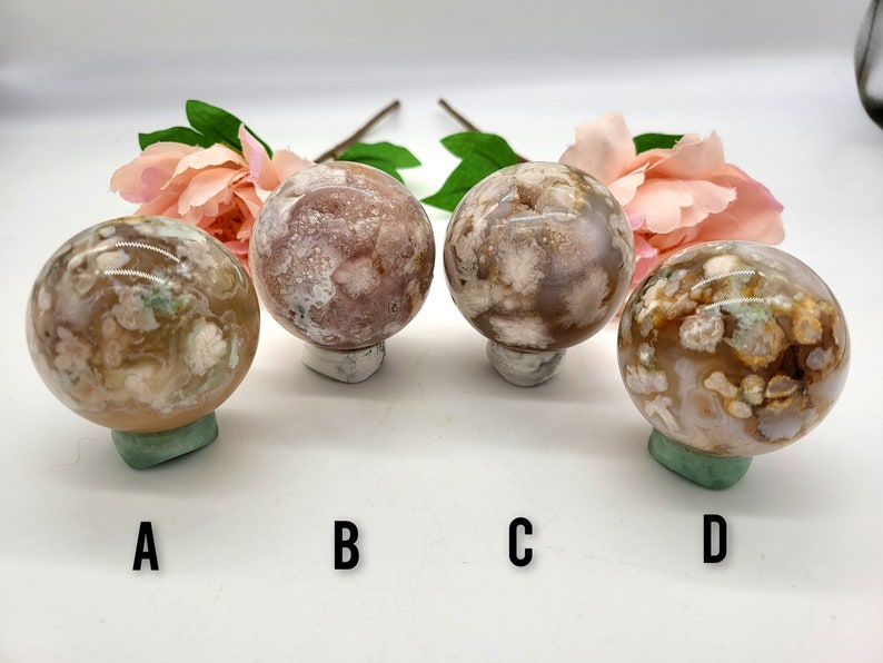 May include: Four agate spheres with different patterns of brown, white, and pink. The spheres are displayed on small stands.