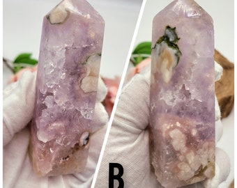 May include: Two purple amethyst crystal points with green and white inclusions. The crystals are polished and have a pointed tip. The crystals are displayed on a white surface.