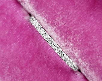 May include: A thin silver band with small diamonds set in a pave setting. The band is displayed in a pink velvet ring box.