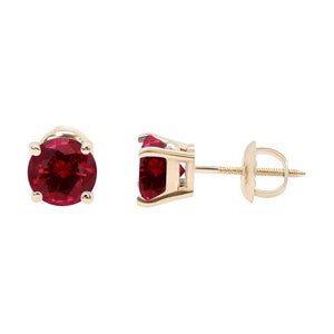 May include: A pair of gold stud earrings with a round red ruby gemstone in each earring.