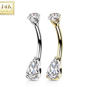 May include: Two curved belly button rings. One is silver-colored, the other is gold-colored. Each ring features a pear-shaped, clear gemstone at the bottom and a round, clear gemstone at the top. The upper left corner of the image has a gold square with the text "14K GOLD".