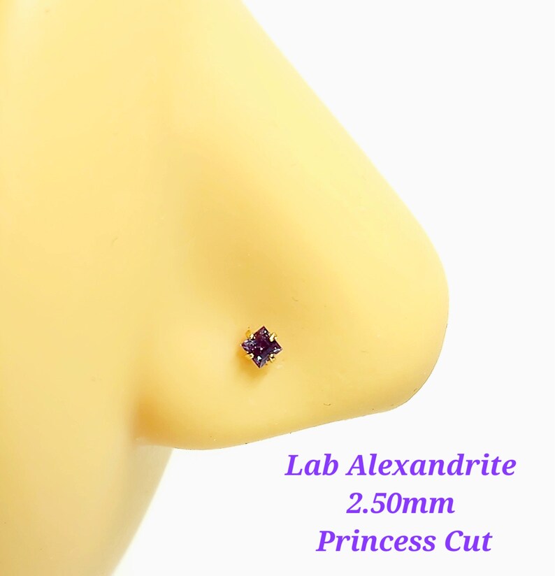 May include: A close-up of a purple lab-created alexandrite nose stud with a princess cut. The stud is 2.50mm in size and is set in gold.