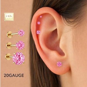May include: Gold-colored, 20-gauge ear studs with pink gemstones. The image shows three studs with a square-cut pink gemstone and a flat back, along with a close-up of an ear with multiple piercings, each with a pink gemstone stud.
