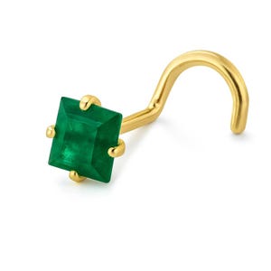 Puede incluir: Un piercing de nariz dorado con una gema verde esmeralda de corte cuadrado. El piercing tiene un poste curvo. La gema está sujeta por cuatro pequeñas garras.