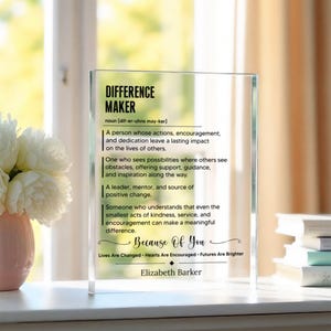 May include: A rectangular clear acrylic plaque featuring black printed text that defines the term Difference Maker. The text includes a phonetic pronunciation, a multi-line definition, the phrase Because Of You, and the name Elizabeth Barker.