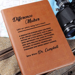 May include: A brown leather journal with the words "Difference Maker" embossed on the front. The journal also includes the definition of the word "Difference Maker" and the text "See Also: Dr. Campbell".
