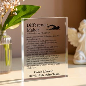 May include: A clear acrylic block with the words "Difference Maker" and a definition, along with a swimmer silhouette. The text includes a dedication to swim coaches, with the coach's name and team at the bottom.