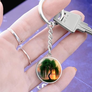 May include: A silver keychain with a round glass charm featuring a weeping willow tree silhouette against a sunset background.