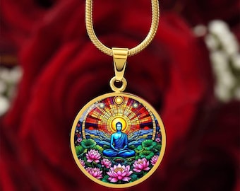 May include: A gold-toned necklace featuring a circular pendant with a colorful stained-glass style illustration of a blue Buddha figure meditating in a lotus position, surrounded by pink lotus flowers and a radiant sunburst pattern in the background.