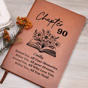 Könnte beinhalten: Ein beigefarbenes Journal in Lederoptik mit dem schwarzen Text Chapter 90, einer Grafik eines offenen Buches mit Blumen, dem Namen Emily und dem Zitat Behind You, All Your Memories, Before You, All your Dreams, Around You, All Who Love You, Within You, All You Need.