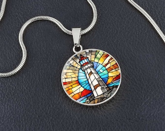 May include: A silver chain necklace with a round pendant featuring a stained glass style lighthouse with a red roof and white stripes against a colorful sunset background.