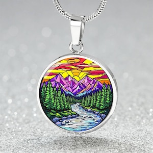 May include: A silver necklace with a round pendant featuring a colorful stained glass style image of a mountain landscape with a river flowing through it. The mountains are purple, pink, and blue, and the sky is orange and yellow.