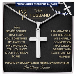 May include: A silver cross necklace in a black box with a heartfelt message for a husband. The message reads "John, Never forget that I love you. Sometimes it's hard to find words to tell you how much you mean to me. I am grateful for the bond we share, a connection that grows deeper with each passing moment. You are my soulmate, best friend, my everything! Love Always, Rebecca."