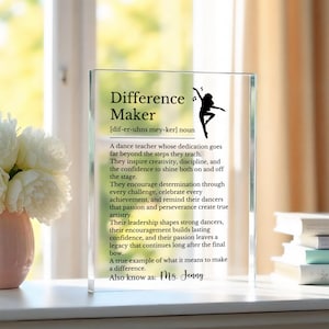 May include: A clear glass plaque with the words "Difference Maker" and a definition of a dance teacher. A silhouette of a dancer is on the right. The text also includes "Ms. Jenny".