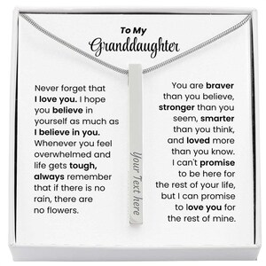 May include: A silver necklace with a vertical bar pendant. The pendant has the text "Your Text here" and is presented in a white box with a message to a granddaughter. The message includes inspirational text.