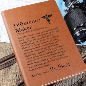 May include: A brown leather journal with the words "Difference Maker" and a definition printed on the cover. A medical symbol is above the text. The journal also includes the name "Dr. Brown".