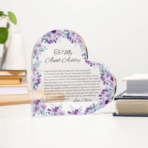 Puede incluir: Placa acrílica en forma de corazón con detalles florales en tonos morados y blancos. El texto dice "To My Aunt Ashley" e incluye un mensaje sincero. Un regalo atento para una tía.