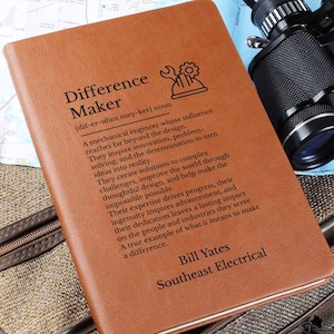 May include: A tan leather-like notebook featuring a black printed definition of Difference Maker, a mechanical engineer icon, and the personalized text Bill Yates Southeast Electrical. The cover has a smooth texture and rectangular shape.