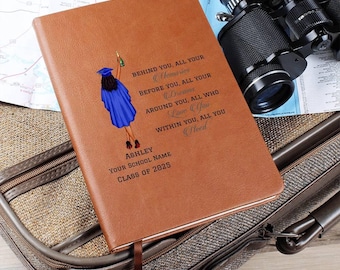 May include: A brown leather-bound journal with a graduation-themed illustration and text. The journal features a blue-robed graduate and the inscription "Behind you, all your memories..." along with a name, school, and graduation year.