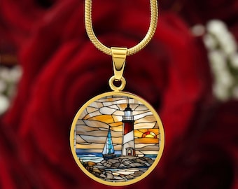 May include: A gold chain necklace with a round pendant featuring a stained glass design of a lighthouse with a sailboat in front of it. The lighthouse is red and white with a yellow light at the top. The sailboat is blue and white. The background is a sunset with orange, yellow, and blue colors.
