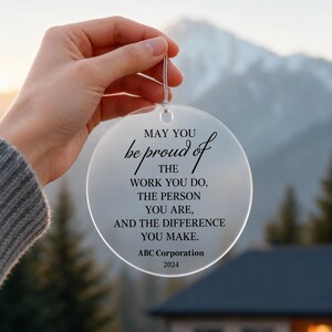 Peut inclure: Un ornement circulaire en acrylique transparent avec un texte imprimé en noir : MAY YOU be proud of THE WORK YOU DO, THE PERSON YOU ARE, AND THE DIFFERENCE YOU MAKE. ABC Corporation 2024. L'ornement comprend une ficelle de suspension argentée.