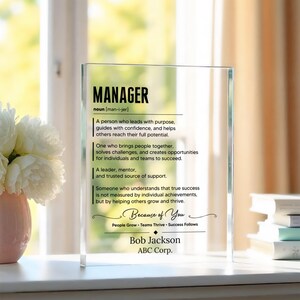 Puede incluir: Una placa rectangular de acrílico transparente con texto impreso en negro que define el sustantivo MANAGER. El texto incluye una definición, la frase Because of You y el nombre Bob Jackson con ABC Corp. en la parte inferior.