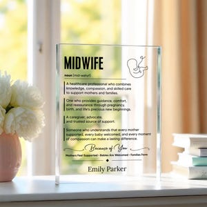 May include: A clear rectangular acrylic plaque featuring black printed text defining the word Midwife. The design includes a line drawing of a fetus, descriptive text about the profession, the phrase Because of You, and the name Emily Parker.