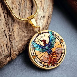 May include: A gold chain necklace with a round pendant featuring a stained glass style phoenix with blue, red, orange, and yellow colours.
