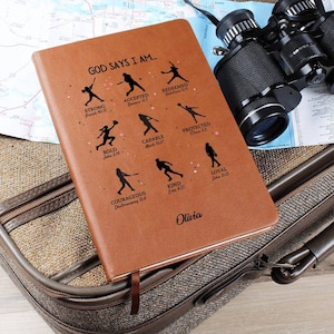 May include: Brown leather journal with a baseball theme. The cover features a silhouette of a baseball player with the words "God Says I Am..." and bible verses. The name "Olivia" is printed at the bottom.