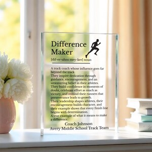 May include: A rectangular clear glass plaque featuring black printed text that defines the term Difference Maker as a track coach. The design includes a silhouette of a runner, a phonetic pronunciation guide, and the name Coach Johnson Avery Middle School Track Team.