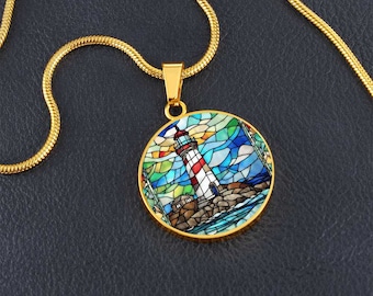 May include: A gold-toned necklace featuring a circular pendant with a stained-glass style illustration of a red and white lighthouse on a rocky shore, surrounded by blue and green geometric shapes, suspended from a matching gold-toned chain.