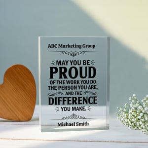 Könnte beinhalten: Ein klarer Acrylblock mit dem Text "MAY YOU BE PROUD" und anderen inspirierenden Worten. Der Block ist mit dem Namen "Michael Smith" und dem Firmennamen "ABC Marketing Group" personalisiert.