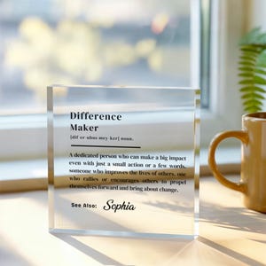 May include: A clear acrylic block with the definition of "Difference Maker" printed in black. The definition includes the pronunciation and a description of a person who makes a big impact. The name "Sophia" is also included.