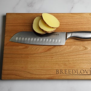 May include: A wooden cutting board with the words "BREEDLOVE" engraved on it. A silver knife and sliced potatoes are on the board.