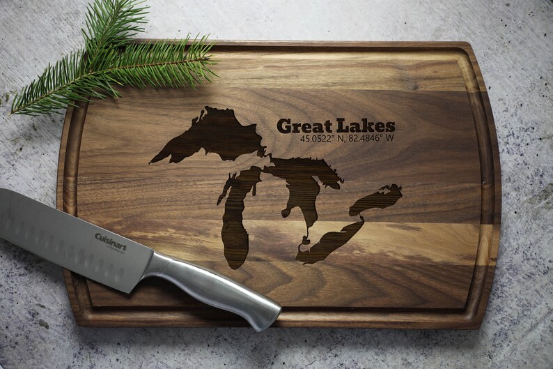 K&ouml;nnte beinhalten: Ein Schneidebrett aus Holz mit einer eingravierten Karte der Gro&szlig;en Seen. Das Brett ist braun und hat eine abgerundete Kante. Der Text "Great Lakes 45.0522&deg; N, 82.4846&deg; W" ist in das Brett graviert.