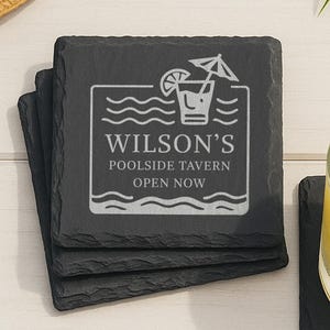 May include: A stack of four square black slate coasters. The top coaster features a white graphic of a cocktail with an umbrella, waves, and the text "Wilson's Poolside Tavern Open Now."