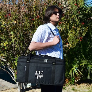 Puede incluir: Una bolsa isotérmica negra con un monograma personalizado de la letra "W" y el nombre "WILLIAMS" en blanco. La bolsa tiene una correa para el hombro y una cremallera.