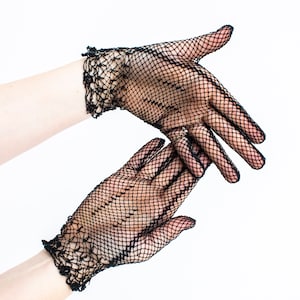 Puede incluir: Un par de guantes de rejilla negra con un delicado ribete de encaje. Los guantes se muestran en un par de manos, con los dedos extendidos.