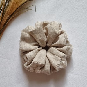 Peut inclure: Un chouchou en tissu beige avec une délicate bordure en dentelle. Le chouchou est fait d'un tissu doux et texturé et a une apparence plissée et bouffante.