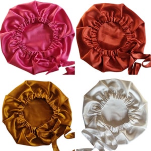 May include: Four satin bonnets in shades of pink, rust, gold, and ivory. Each bonnet has a gathered elastic edge and long ties for securing. The bonnets are designed to protect hair while sleeping or during other activities.