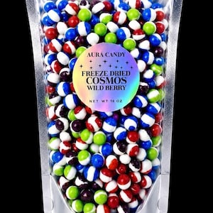 May include: A clear, resealable stand-up pouch filled with small, round, multi-colored candies in red, blue, green, and white. A circular, iridescent label on the front reads: AURA CANDY, FREEZE DRIED COSMOS, WILD BERRY, NET WT 16 OZ.