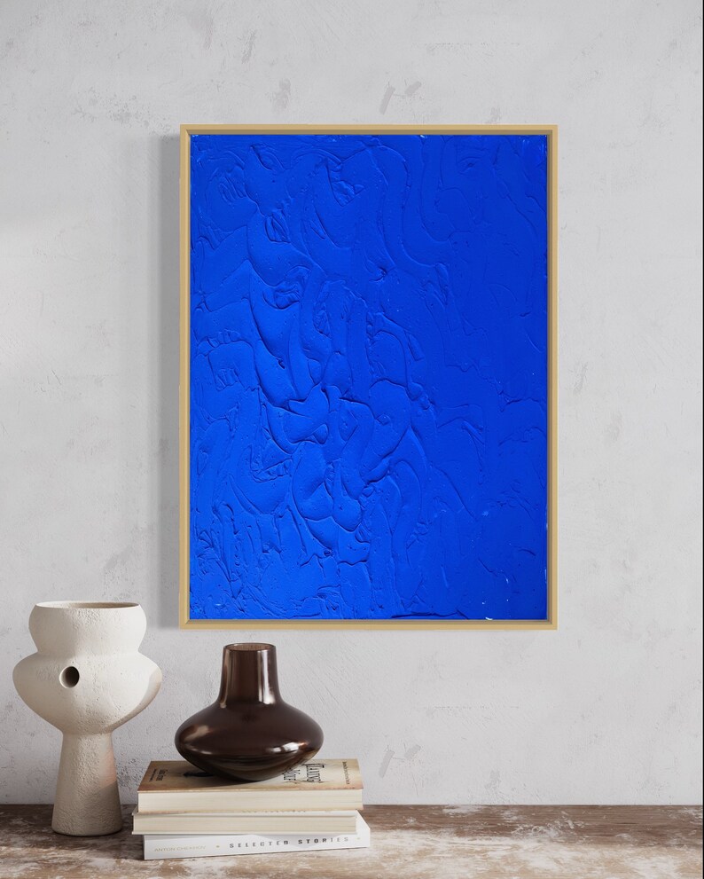May include: A framed abstract painting with a textured blue background. The painting is in a gold frame and is hanging on a white wall.