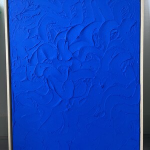May include: A framed abstract painting with a textured blue surface. The painting is in a wooden frame.
